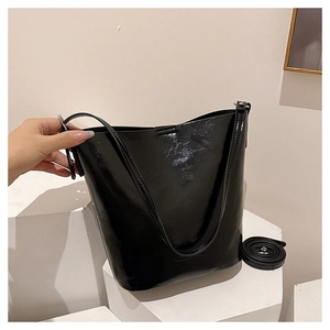 Detail of glossy black patent leather bucket bag with dual straps on white stone display