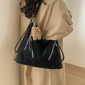 Detail of black large capacity shoulder bag with decorative zippers and plush dog charm