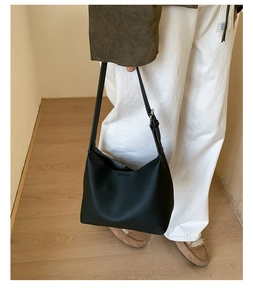 Detail of minimalist black pebbled leather bucket bag with adjustable strap and hobo shape