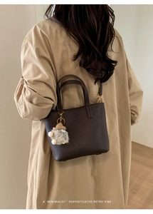 Detail of dark brown lychee leather bucket bag with cute plush pendant and shoulder strap