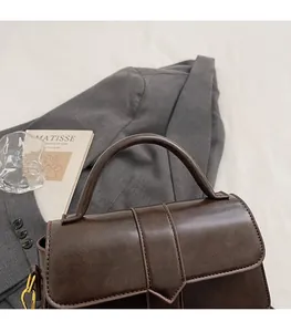 Detail of dark brown leather handbag featuring V-shaped flap and gold metal hardware