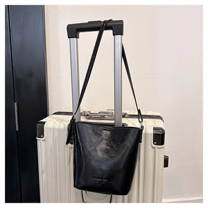 Detail of a black glossy leather bucket bag hanging on a suitcase handle