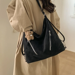 Detail of a large black matte crossbody bag with silver zippers and a brown bear pendant