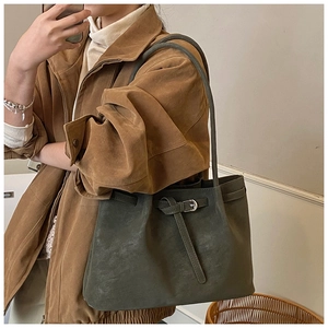 Detail view of a dark gray-green tote bag with belt buckle closure on a suede coat model