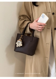 Deep brown pebble leather bucket bag with plush charm shown in a minimalist street style