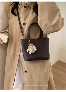 Detail of dark brown pebble leather bucket bag with cute plush pendant and top handle