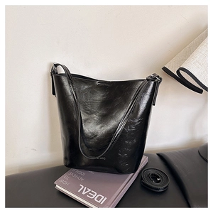 Detailed view of black glossy bucket bag with stylish detachable strap on a fashion book