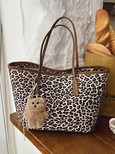 Large leopard print tote bag with brown straps and plush bear charm on a wooden table