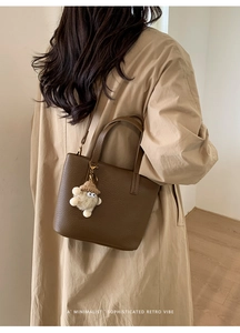 Model wearing dark brown lychee textured bucket bag with plush charm on a beige trench coat