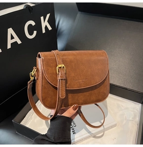 Detail of a brown leather crossbody bag with vintage texture and gold buckle in a box
