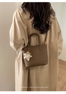 Detail of dark brown pebble leather bucket bag with cute charm and long strap on model