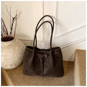 Detail of dark brown matte tote bag featuring decorative straps and metal buckles