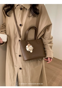 Brown litchi grain bucket bag with monster plush pendant on khaki trench coat background