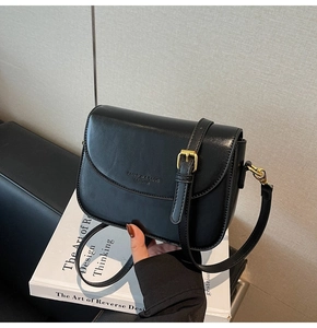 Detail view of black glossy leather shoulder bag with gold adjustable buckle on a book