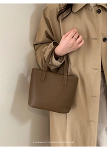 Detail of dark brown litchi grain leather bucket bag held by a model in khaki trench coat