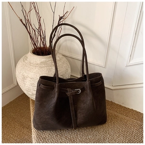 Detail of dark brown suede tote bag with slim decorative straps and metal buckles