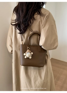 Detail of dark brown lychee leather tote bag with cute doll charm and crossbody strap