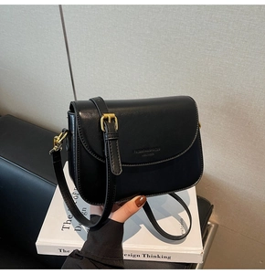 Detail of minimalist black leather shoulder bag showing embossed logo and gold hardware