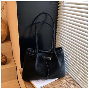 Close-up of black matte tote bag with slim strap and metal buckle under shutter shadows