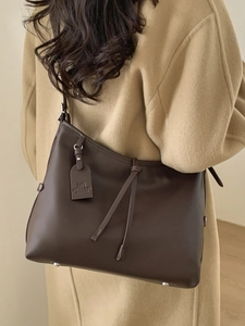 Grand sac cabas en cuir marron foncé avec pieds en métal porté par un mannequin en manteau