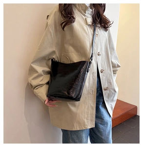 Polished black leather bucket bag worn as a shoulder bag in a minimalist setting