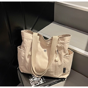 Detail view of large beige canvas tote bag with side hidden pocket and metal logo