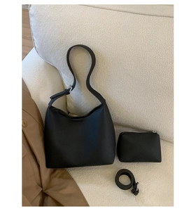 Close-up of black pebble leather hobo bucket bag set with mini pouch and strap on sofa