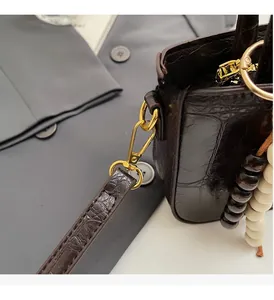 Detail of dark brown crocodile texture leather bag with gold hardware and bead charm