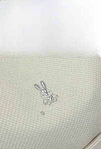 Macro shot of a textured cream backpack featuring a silver metal rabbit logo and brand text