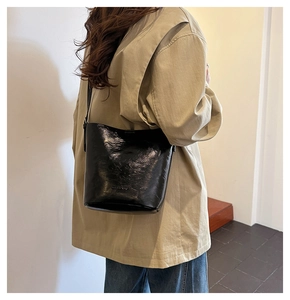 Side view of a black glossy bucket bag worn over the shoulder on a khaki shirt