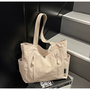 Detail view of beige canvas tote bag with functional zippers and black brand label