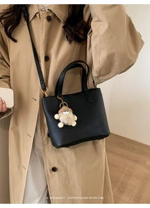 Detail of black lychee grain leather handbag with cute plush charm and gold hardware