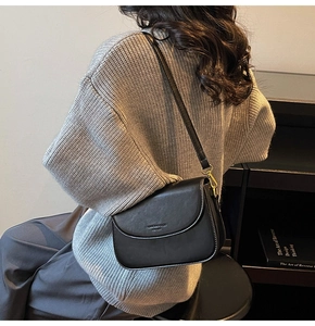 Detail of black leather crossbody bag with gold hardware and logo on a grey sweater