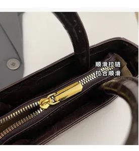 Detailed macro view of the gold metal zipper on a burgundy crocodile texture handbag