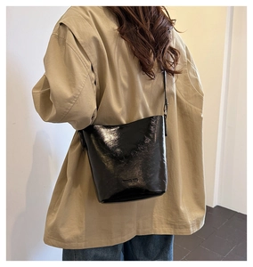 Model wearing black patent leather bucket bag with adjustable strap and textured finish