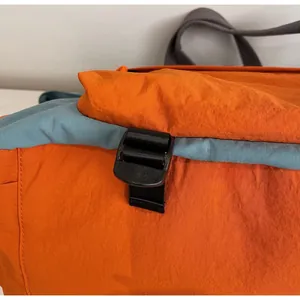 Dettaglio della fibbia in plastica nera e della cinghia in nylon sulla borsa da viaggio arancione