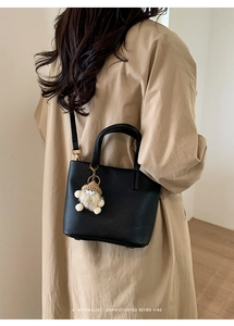 Detail of black pebbled leather bucket bag with a cartoon charm on a khaki coat