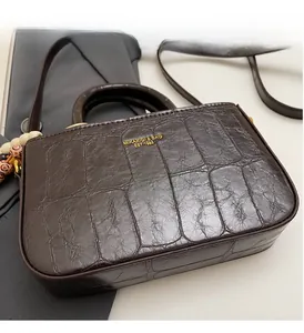 Detailed view of dark brown crocodile embossed leather handbag with gold logo lettering