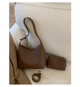 Deep brown pebble leather bucket bag set with matching pouch on a cozy beige sofa
