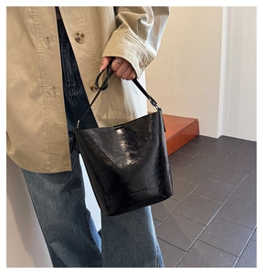 Close-up of black glossy leather bucket bag with embossed logo worn by a model