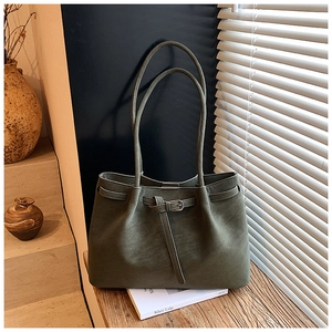 Detail of dark olive green leather tote bag with adjustable buckle strap on wood table
