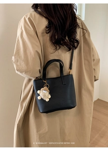 Litchi texture black bucket bag with plush charm shown on person in trench coat