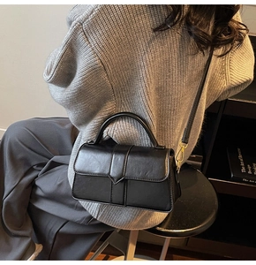 Detail of a black leather crossbody square bag with gold hardware on a model outfit