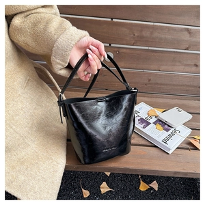Detailed view of a black glossy leather bucket bag on a wooden bench with autumn leaves
