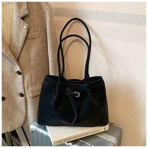 Close-up of black leather tote bag with buckle detail against a minimalist lifestyle background