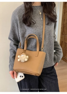 Chic camel faux leather crossbody bag with plush charm shown in a minimalist setting