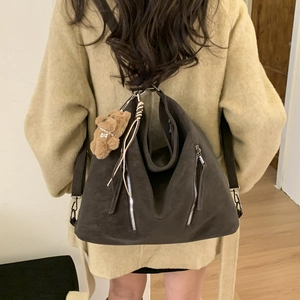 Detail of dark brown slouchy leather backpack showing zipper accents and bear charm