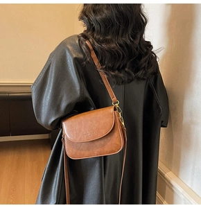 Rear view of model wearing a vintage brown leather crossbody bag with a black coat