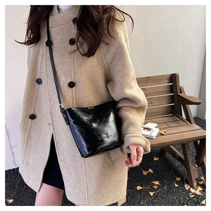 Outdoor lifestyle shot of a black glossy bucket bag worn with a beige wool coat