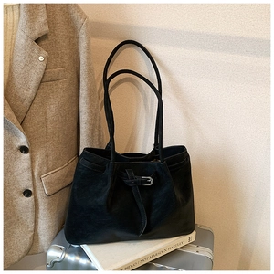 Detail of black pebbled leather tote bag with silver buckle and drawstring on white book